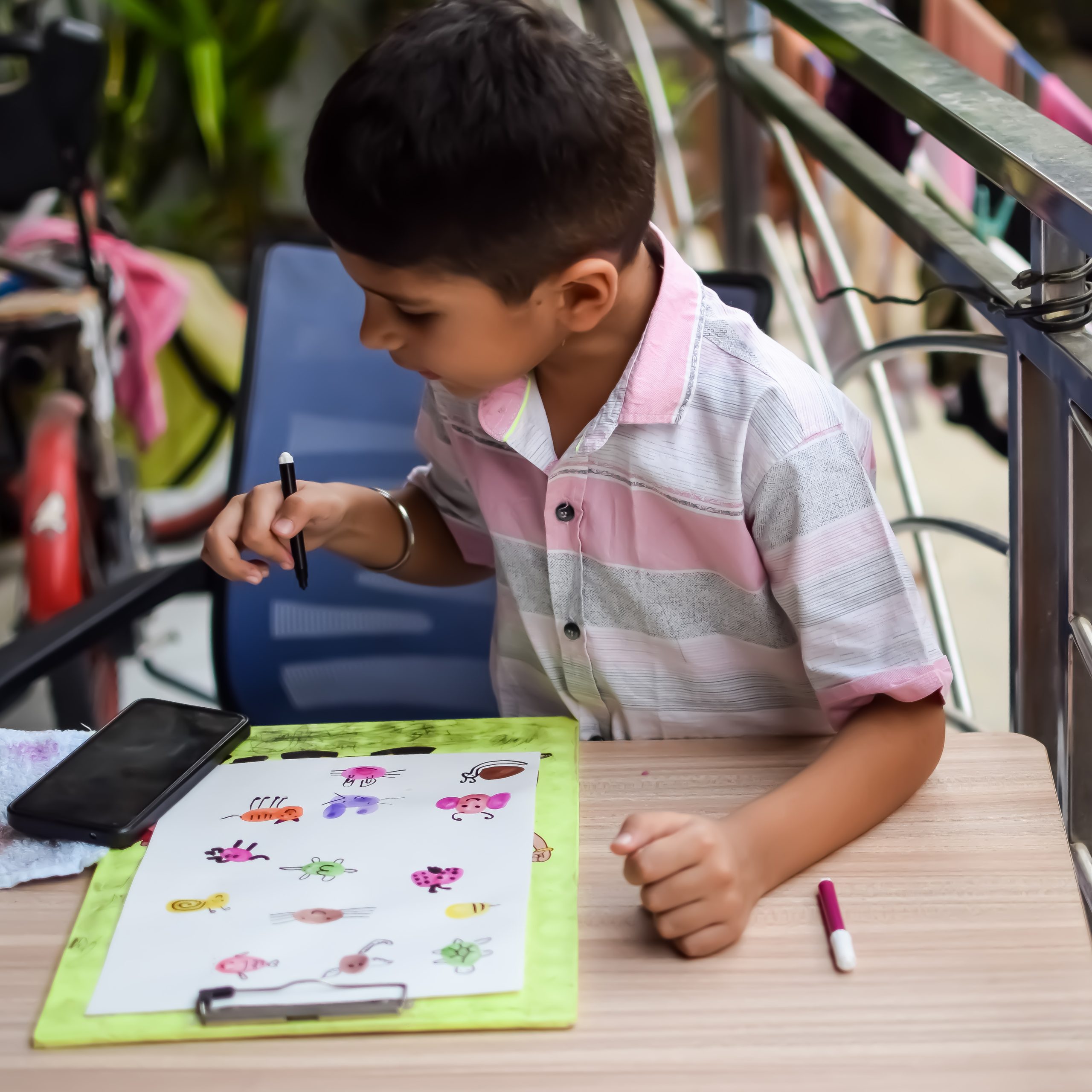 Smart Indian little boy perform thumb painting with different colourful water colour kit during the summer vacations, Cute Indian Kid doing colourful thumb painting drawing on wooden table